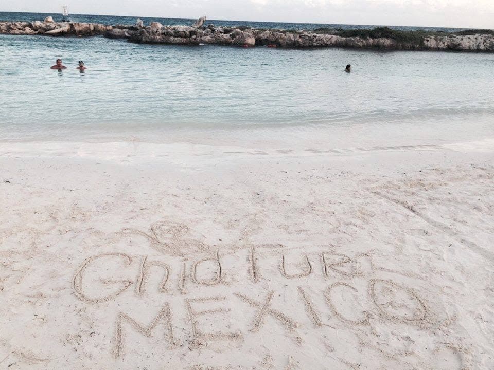 Inscripția „GhidTur Mexico” pe nisip, lângă mare.